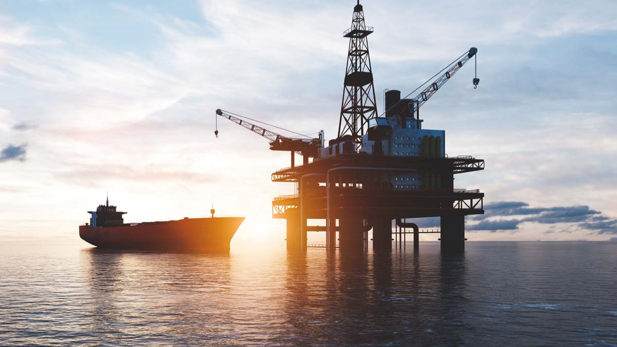 Offshore oil platform and cargo vessel at sunset operating above calm ocean waters.