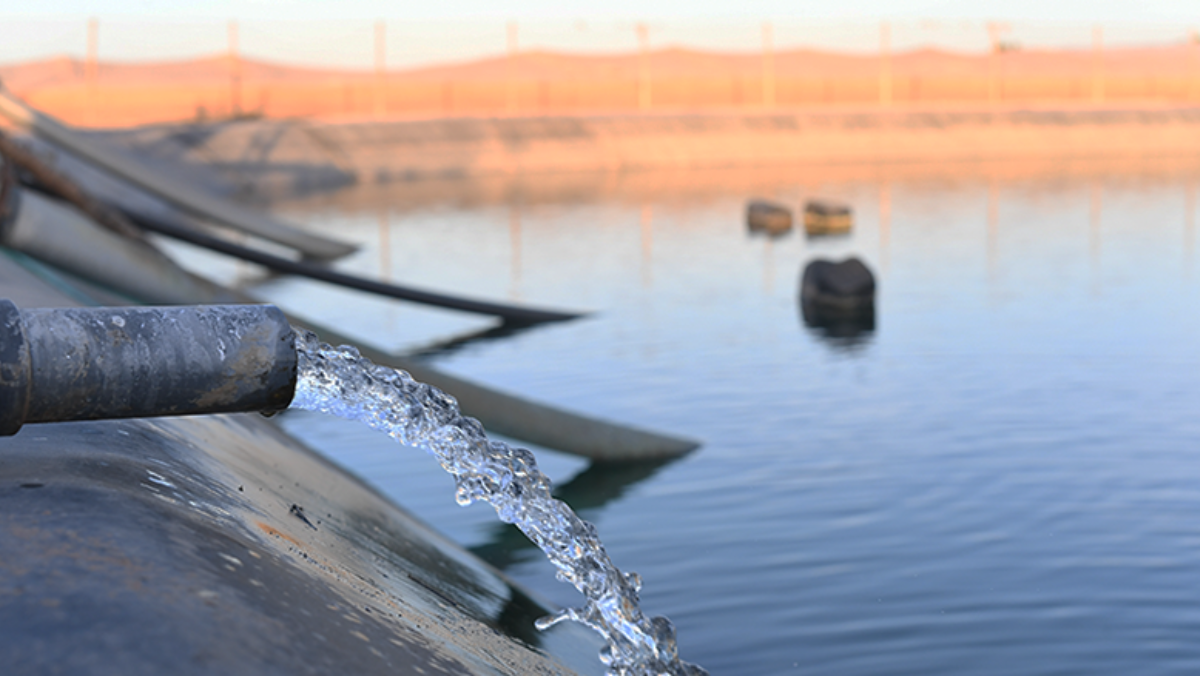 Produced water flowing from pipe into oilfield storage pond