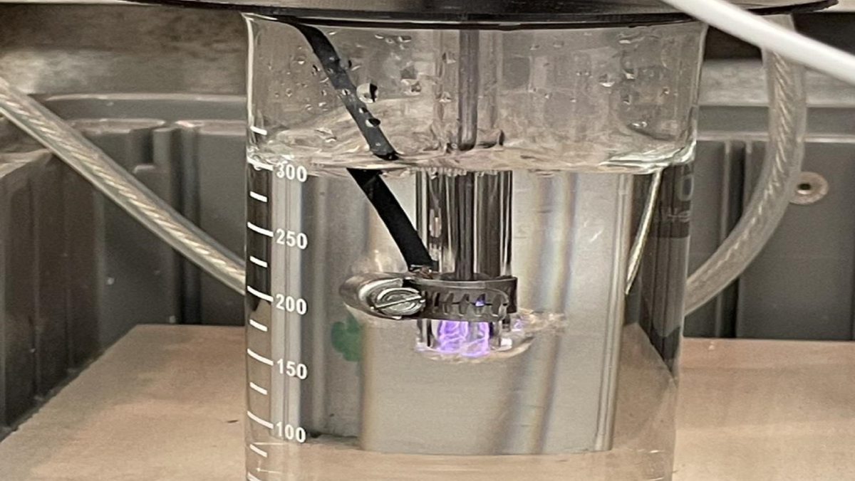 Beaker with submerged plasma probe generating purple glow during produced water treatment test.